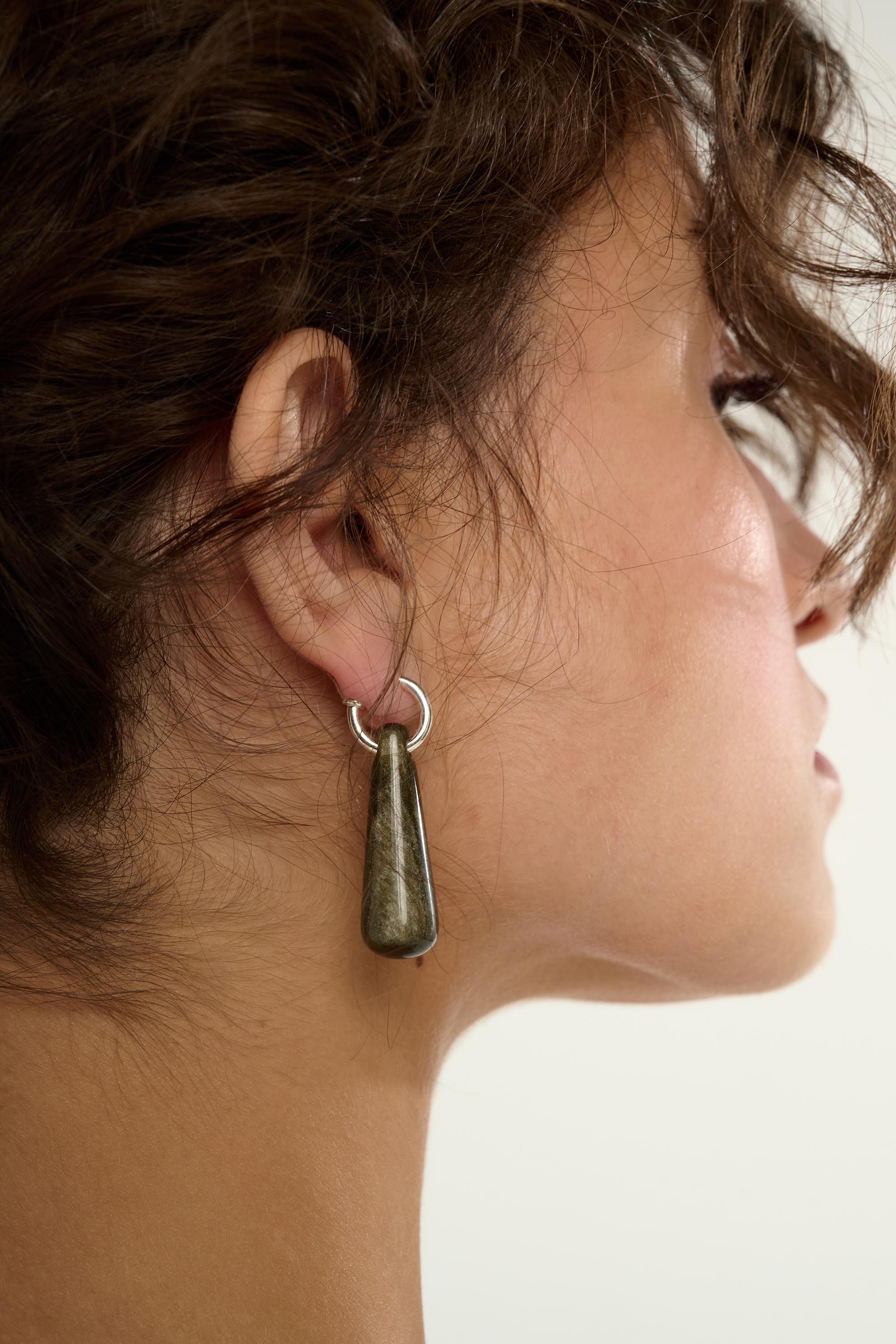 Close-up of a person wearing a dangling earring with a plain background
